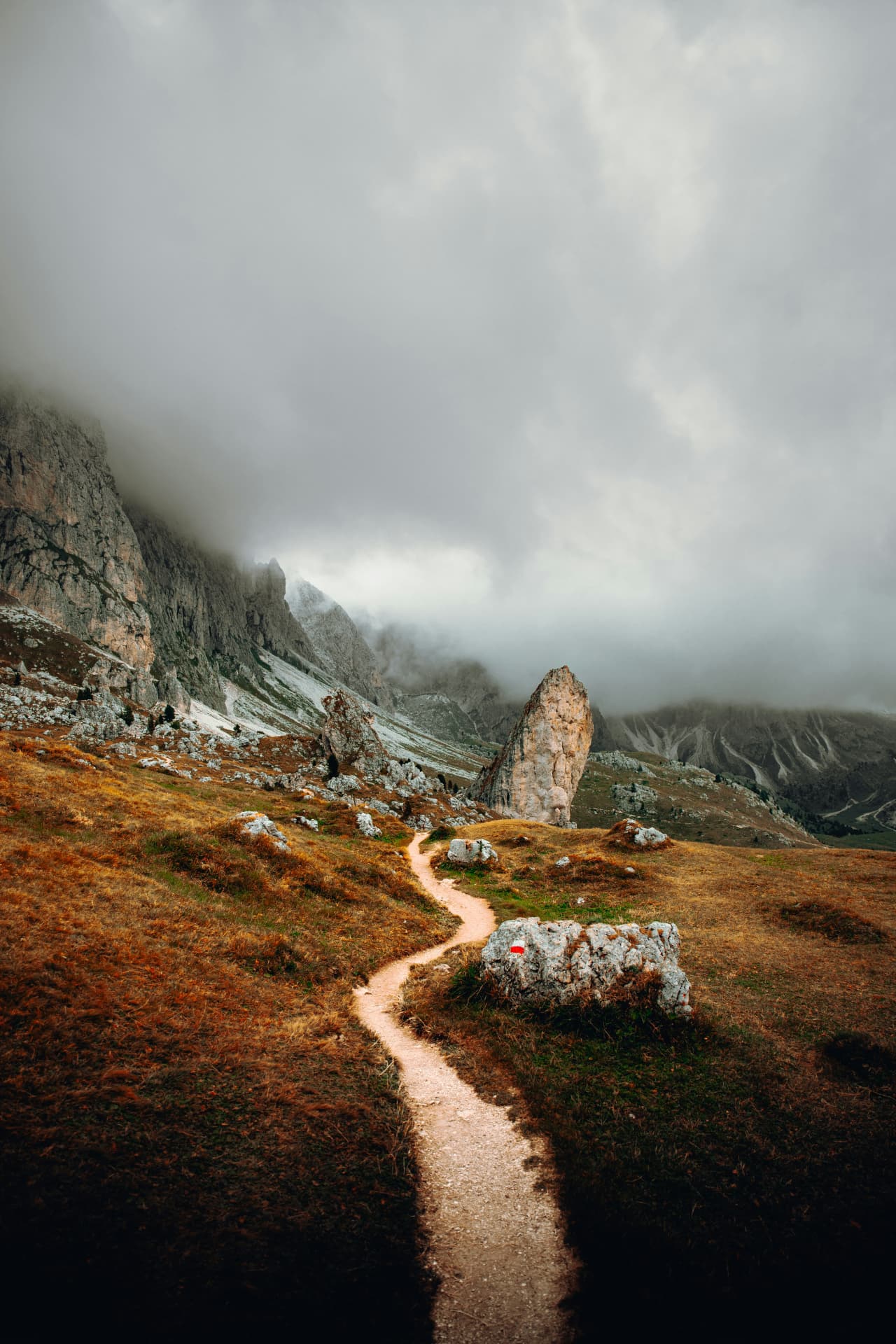 A winding dirt path through an open mountain landscape under a cloudy sky